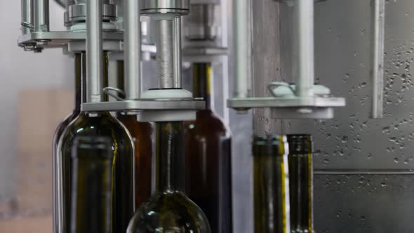 Close-up of factory machine picking up wine bottles and filling them on an automated production line