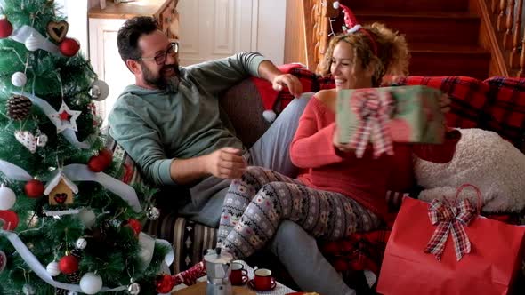 Sharing gift surprise scene with happy adult couple at home during Christmas Eve day