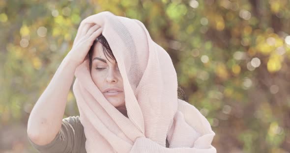 A beautiful brunette model poses with a light scarf on her head outdoors