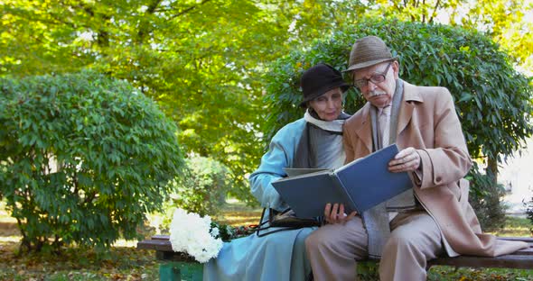 Elderly Couple Looking at a Photo Album When Relaxing on Bench