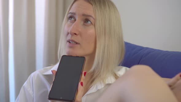 a woman at home records a voice message on her smartphone while lying on bed.