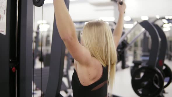 Attractive Young Blond Caucasian Woman with Sporty Body Training Hard on a Lat Pulldown Mashine at