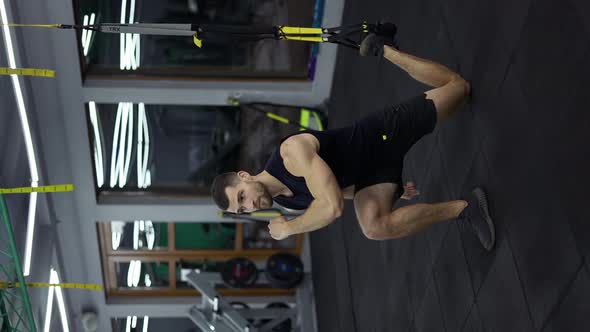 Sportsman Doing Squats Exercises with TRX Straps at Gym
