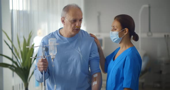 Aged Man Patient with Dropper Talking To Nurse Standing in Hospital Ward