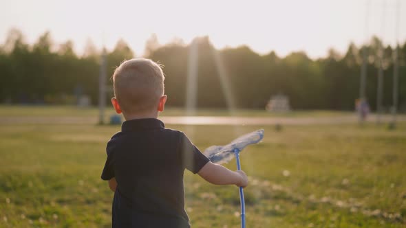 Toddler Boy Runs Holding Butterfly Net Along Meadow