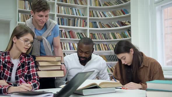Multiracial Students Preparing for Exams in the Library while Their Friend Carring Other Books alt