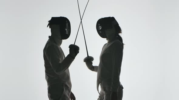 Dark Silhouettes of Two Swordsmen Crossing Swords on a White Background. Close Up. Slow Motion.