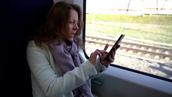 Female Passenger in Suburban Train, Sitting Near Window and Using Smartphone