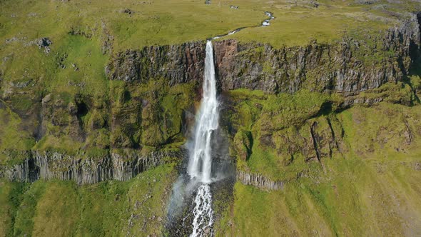 Aerial Drone Footage of Bjarnarfoss Waterfall Mountain Cliffs and Green Plateau in Western Iceland