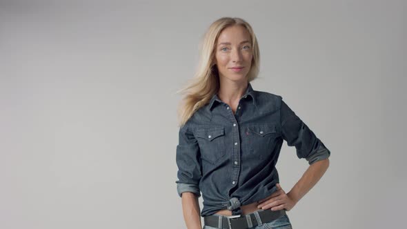 Young Beauty Blonde Woman in Studio Wears Classic Denim with Blowing Hair