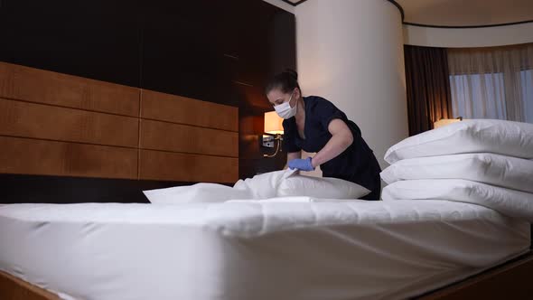 Masked Maid in Gloves Making Bed in Hotel Room
