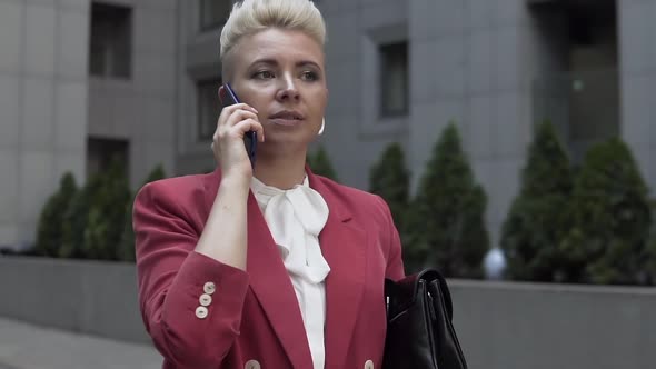 Serious blonde short-haired woman in red jacket is talking on the phone