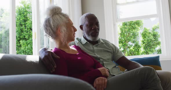 Mixed race senior couple taking to each other while sitting on the couch at home