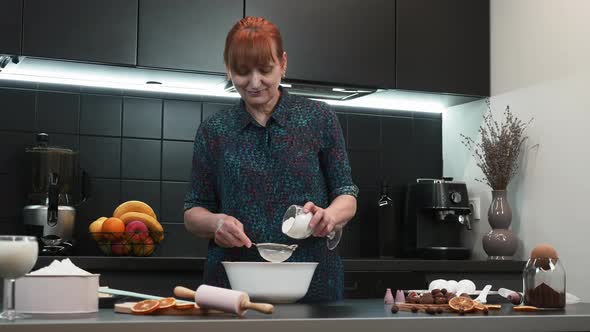 Woman in kitchen. Mature female is cooking cake. 