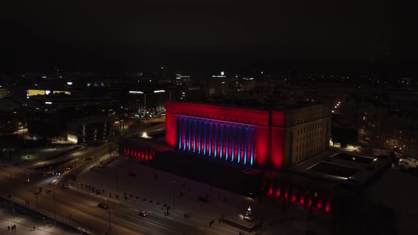 Night aerial retreats from Helsinki Parliament lit up blue and red