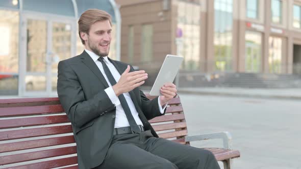 Online Video Chat on Tablet By Businessman Sitting Outdoor on Bench