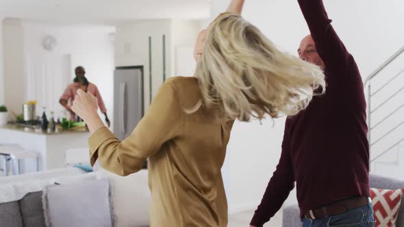 Caucasian senior couple dancing in a living room with senior african american couple in background