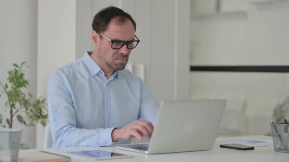 Middle Aged Man Feeling Disappointed While Using Laptop in Office