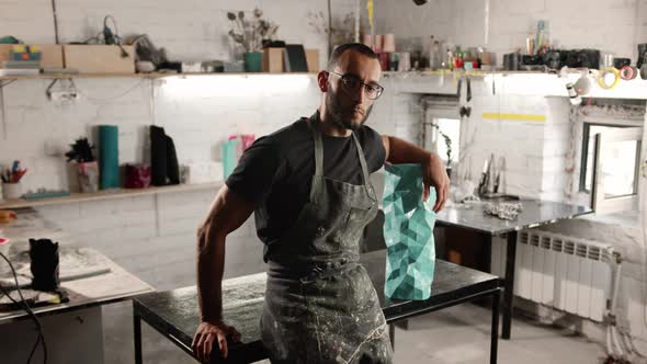 Portrait of a man: a male artisan sculptor looks at the camera against the backdrop of a workshop