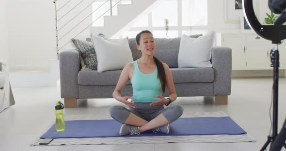 Happy asian woman sitting on mat, making fitness vlog from home