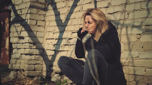 Upset Woman with a Cigarette near a Brick Fence