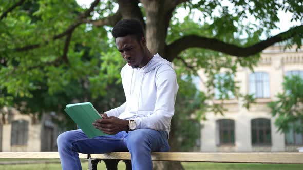 Confident Focused African American Man Surfing Internet on Tablet Drinking Morning Coffee Sitting on