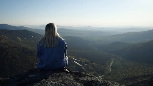 The Blonde in the Denim Jacket Sits on the Edge of the Stone