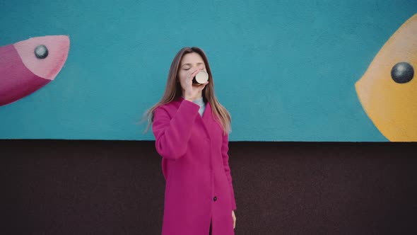 A Girl in a Pink Coat Drinks Coffee and Stretches It to the Camera