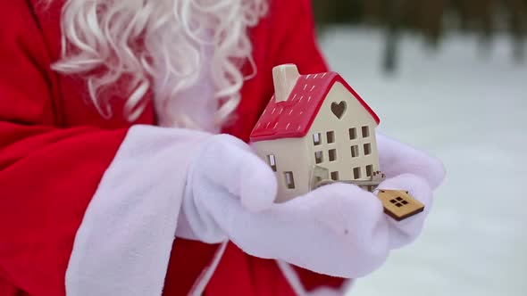 House key with keychain cottage in hands of Santa Claus outdoor in snow. Deal for real estate, purch