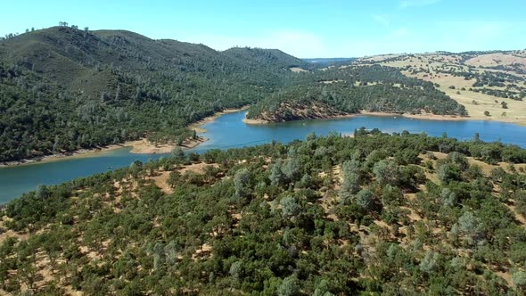 Slowly flying over hills, trees, sand and a curved lake.