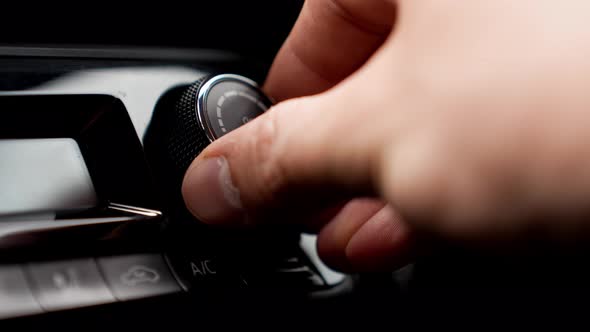 Man's hand turning air condition button wheel to adjust temperature in car.