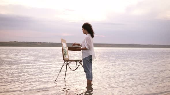 Accelerated Shooting a Girl Artist in the Water Till Ankles Draws a Landscape Using an Easel and a