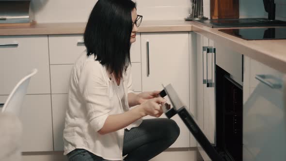 Young Woman Opens Oven Door in Kitchen