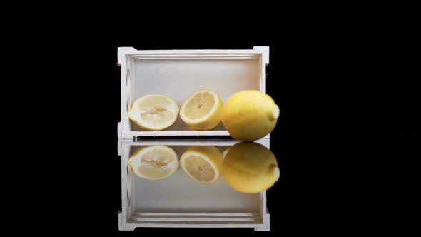 Yellow lemon rolling against white crate with halves of lemons inside