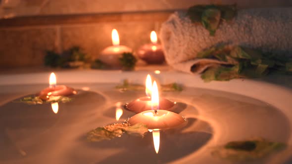 relaxing spa background with candles floating in the bath water, some green petals and a towel near