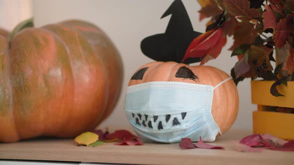 Halloween Decoration Pumpkin with Hat and Protective Medical Mask on Face Stands on Table with