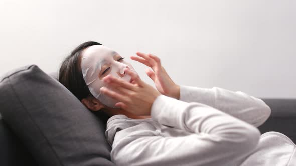 Woman applying facial mask and lying on sofa 