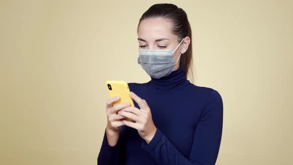 Portrait of Young Woman in Medical Mask Uses Mobile Phone, Isolated Background