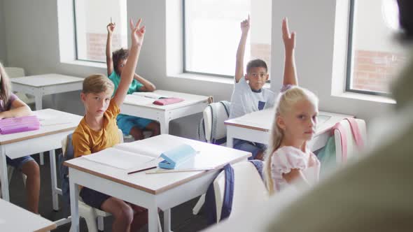 Video of diverse pupils raising hands during lesson in classsroom