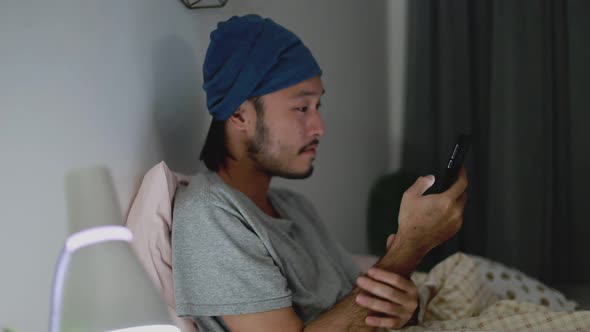 Attractive Asian man using a mobile phone while Lying on Bed at home.