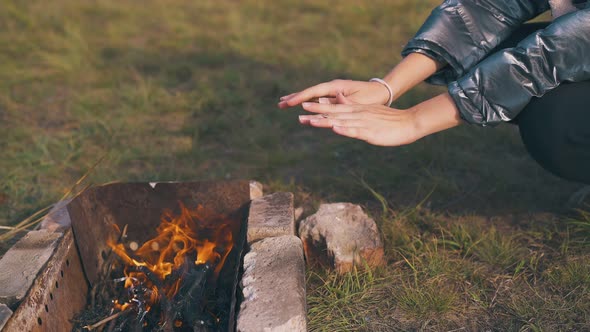 Girl Hiker Heats Hands at Burning Bonfire at Camp Closeup