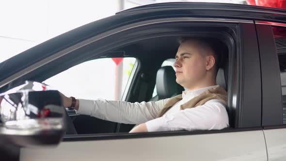 Portrait of a Young Confident Man Sitting in a New Car at a Car Dealership