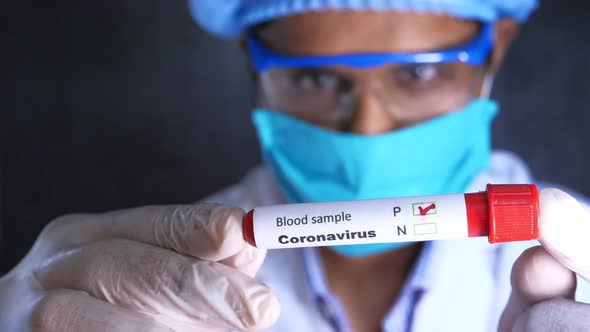 Laboratory Technician in Face Mask and Protective Glass Holding Blood Test Tube 