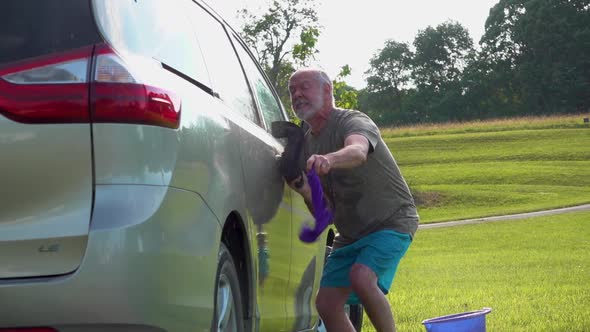 Slow motion of dancing crazy man doing the twist while washing his car with hose and soapy sponges.