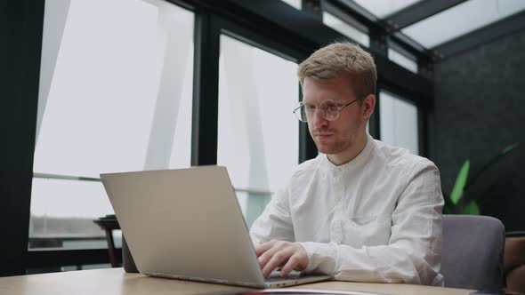 Serious Focused Determined Young Bearded Businessman or Freelancer in Glasses and Typing on Laptop