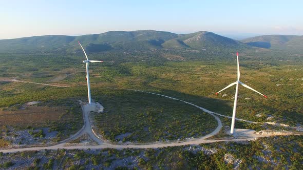 Flying above two elegant white wind turbines on green hills