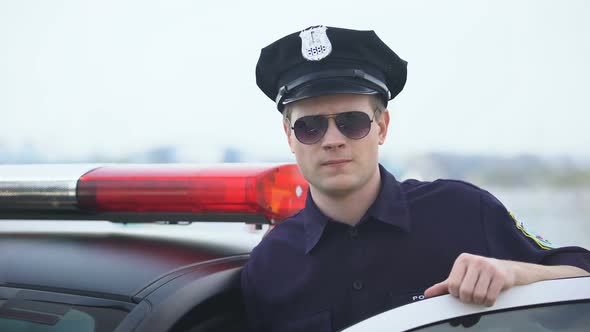 Confident Police Officer in Uniform and Sunglasses Standing Near Patrol Car