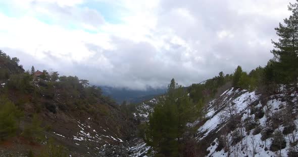 Drone shot entering snowed valley through trees revealing mountains  clouds on horizon