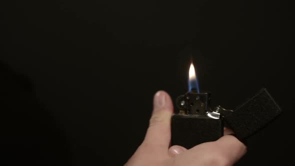 Woman's Hand Ignites Vintage Cigarette Lighter on a Black Background
