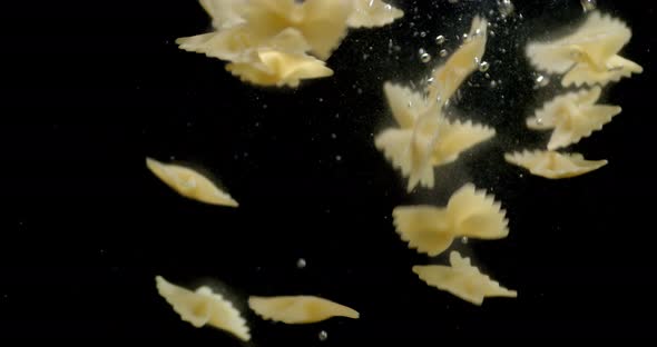 Dry Farfalle Pasta Falls Under Water with Air Bubbles. 